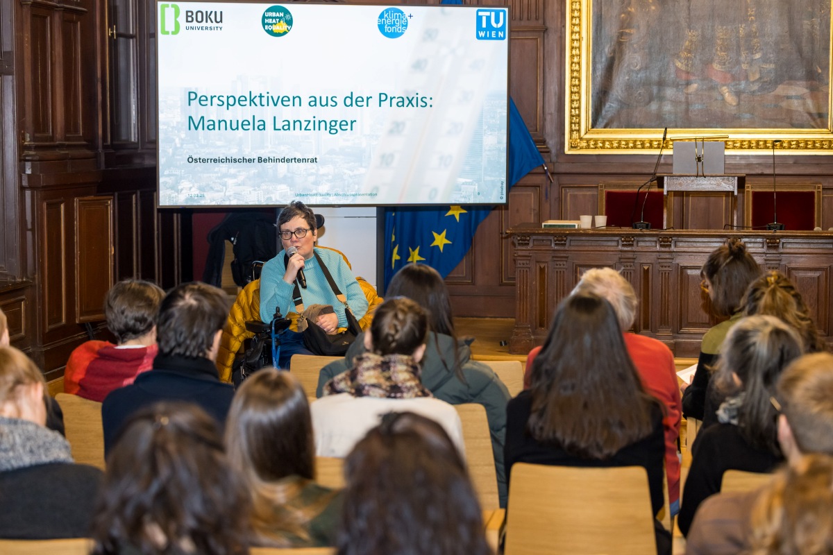 Ein Frau sitzt im Rollstuhl vor Publikum und spricht in ein Mikrofon. Im Hintergrund ist eine Präsentationsfolie mit dem Titel „Perspektiven aus der Praxis: Manuela Lanzinger“ und dem Hinweis auf den Österreichischen Behindertenrat zu sehen. Das Publikum sitzt auf Stühlen und hört dem Vortrag zu