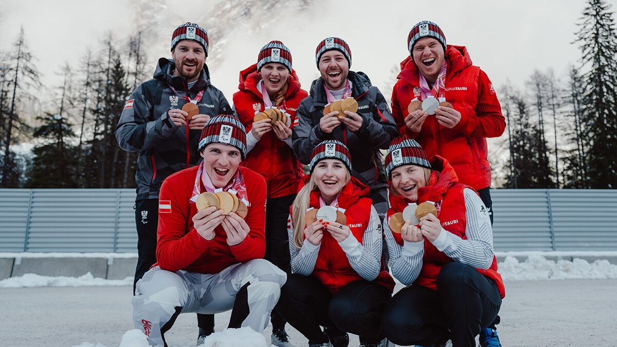 Sieben Athlet*innen des Paralympic Team Austria stehen im Schnee und halten ihre Medaillen der Paralympischen Winterspiele Milano Cortina 2026 in die Kamera.