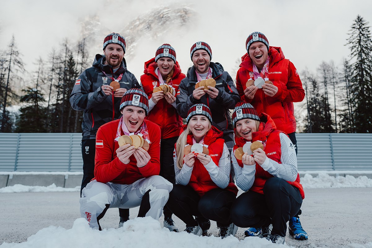 Sieben Athlet*innen des Paralympic Team Austria stehen im Schnee und halten ihre Medaillen der Paralympischen Winterspiele Milano Cortina 2026 in die Kamera.