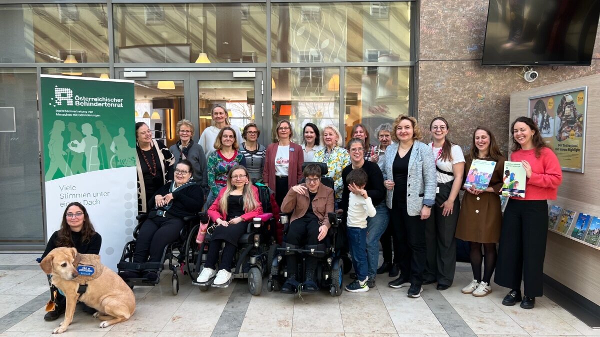 Gruppenbild von etwa 25 Frauen, einem Kind und einem Hund vor dem Rollup des Österreichischen Behindertenrats