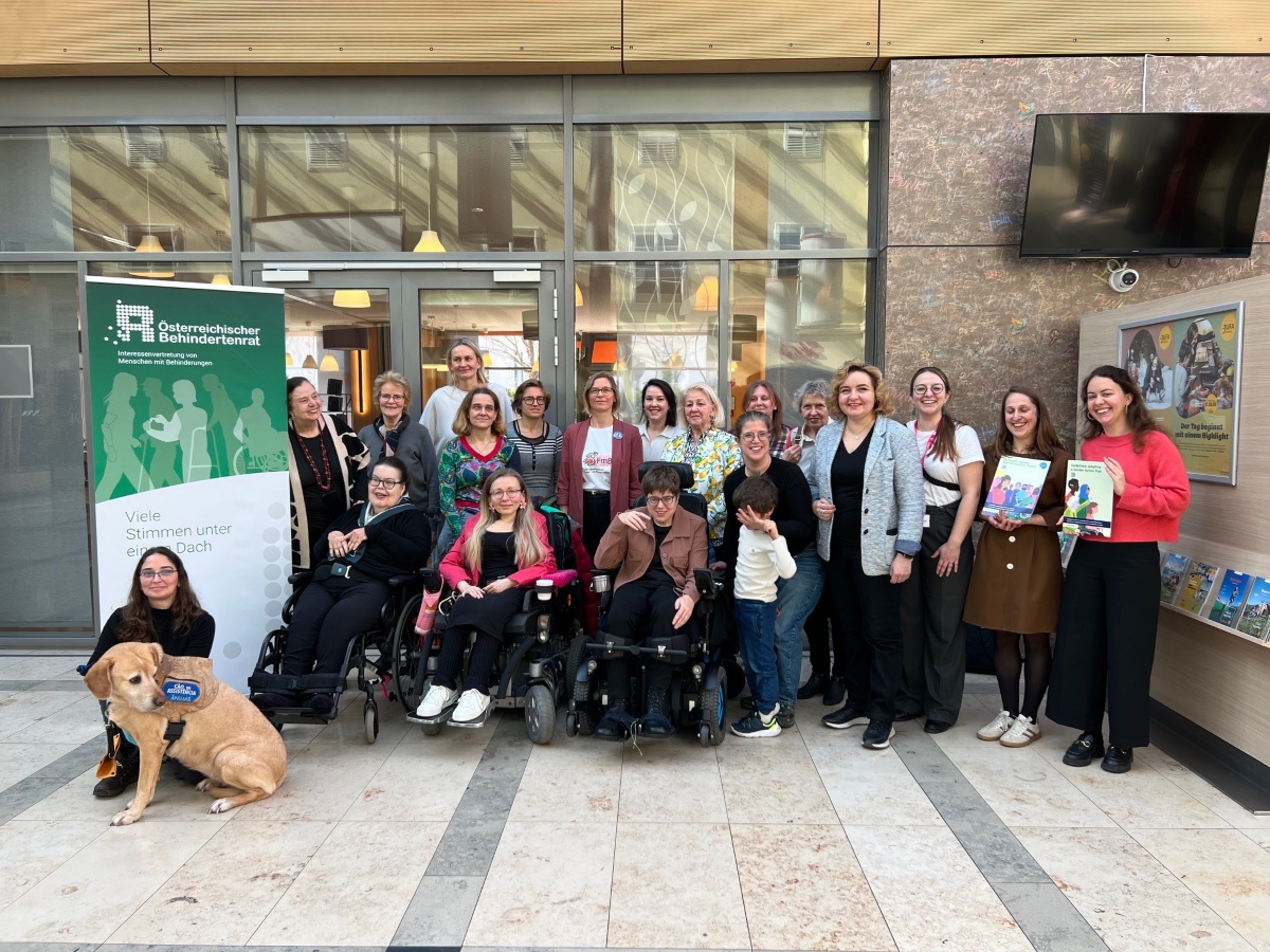 Gruppenbild von etwa 25 Frauen, einem Kind und einem Hund vor dem Rollup des Österreichischen Behindertenrats