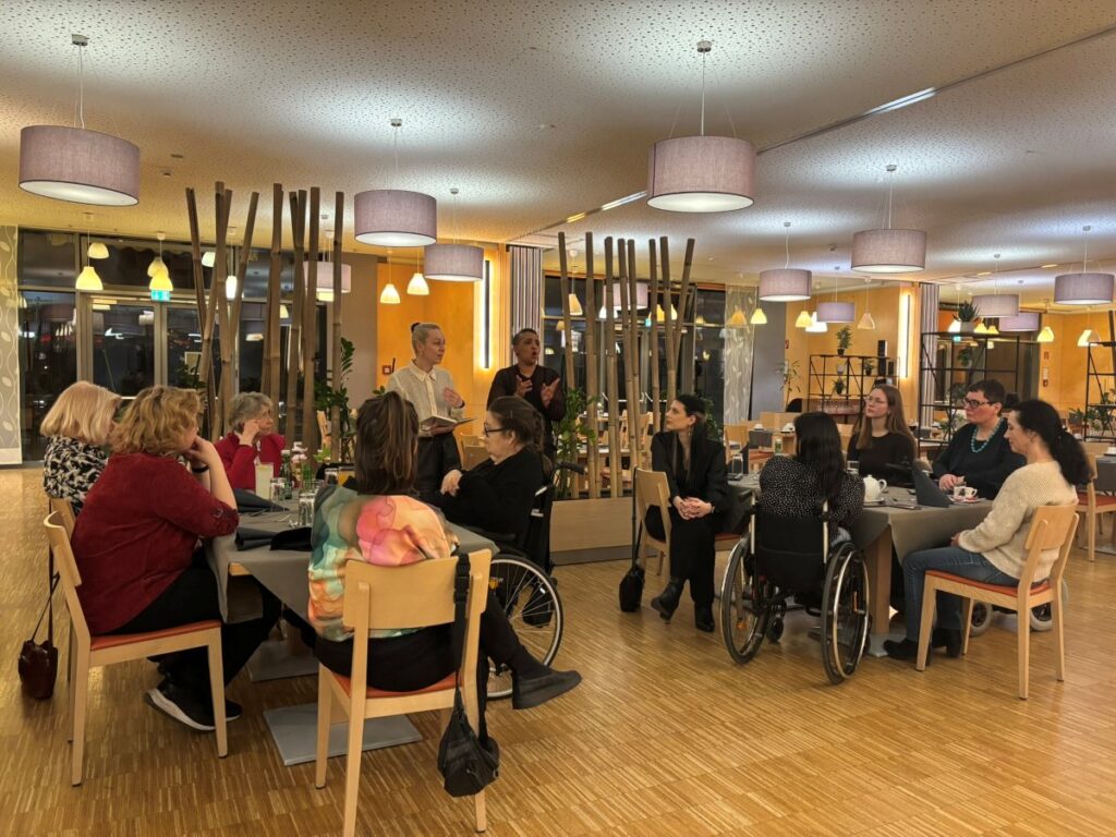 mehrere Frauen sitzen in einem Seminarraum auf Stühlen, im Hintergrund Schriftdolmetschung