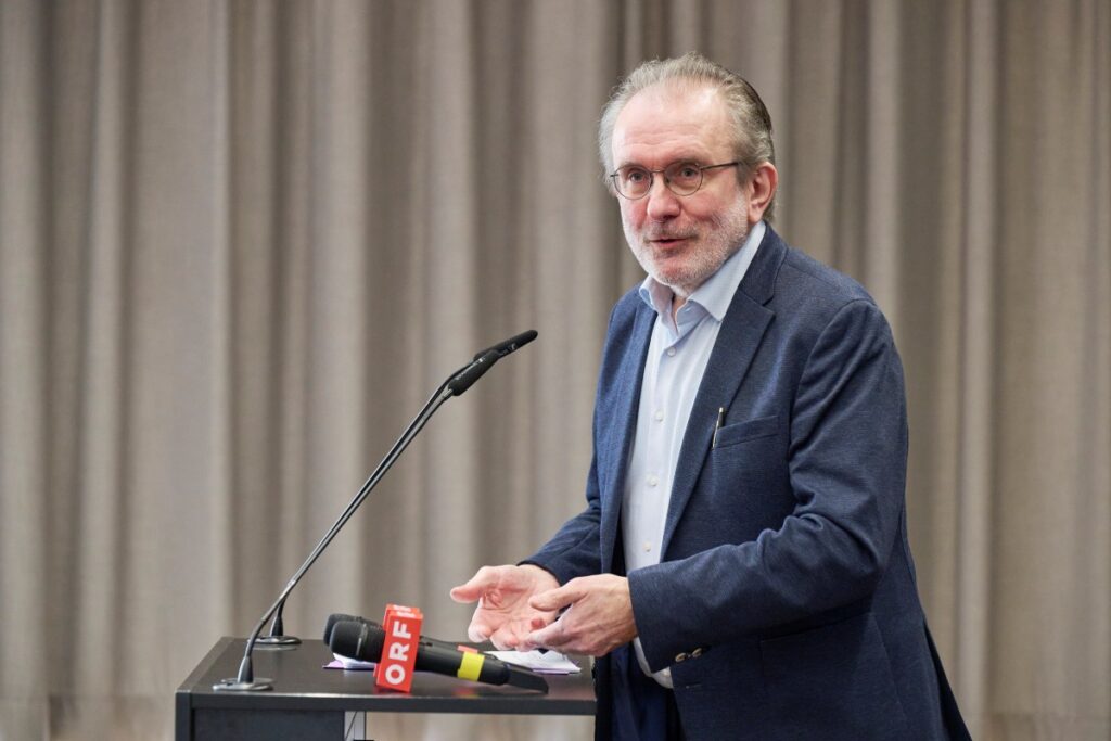 Mann mit grauem Haar, blauem Hemd und blauem Sakko, hält eine Rede
