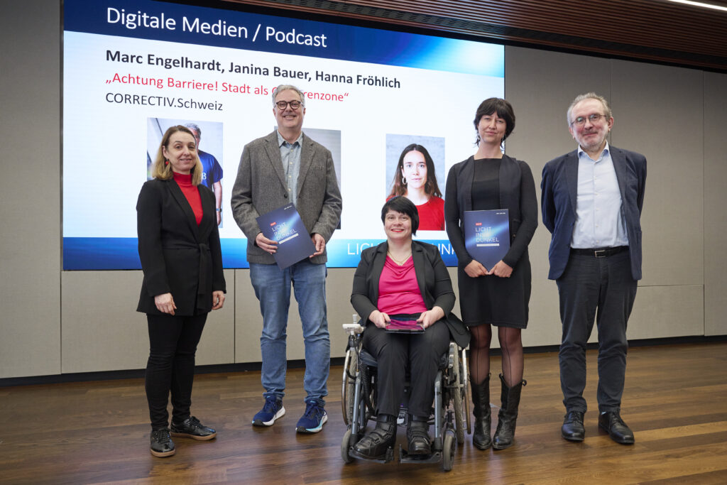 Marc Engelhardt und Janina Bauer werden mit dem Herbert-Pichler-Inklusions-Medienpreis 2026 in der Kategorie Digitale Medien ausgezeichnet. Sie stehen gemeinsam mit Ivana Veznikova, Fritz Hausjell und Ines Stilling auf einer Bühne vor einer Präsentationsfolie mit Titel und Porträts des Beitrags.