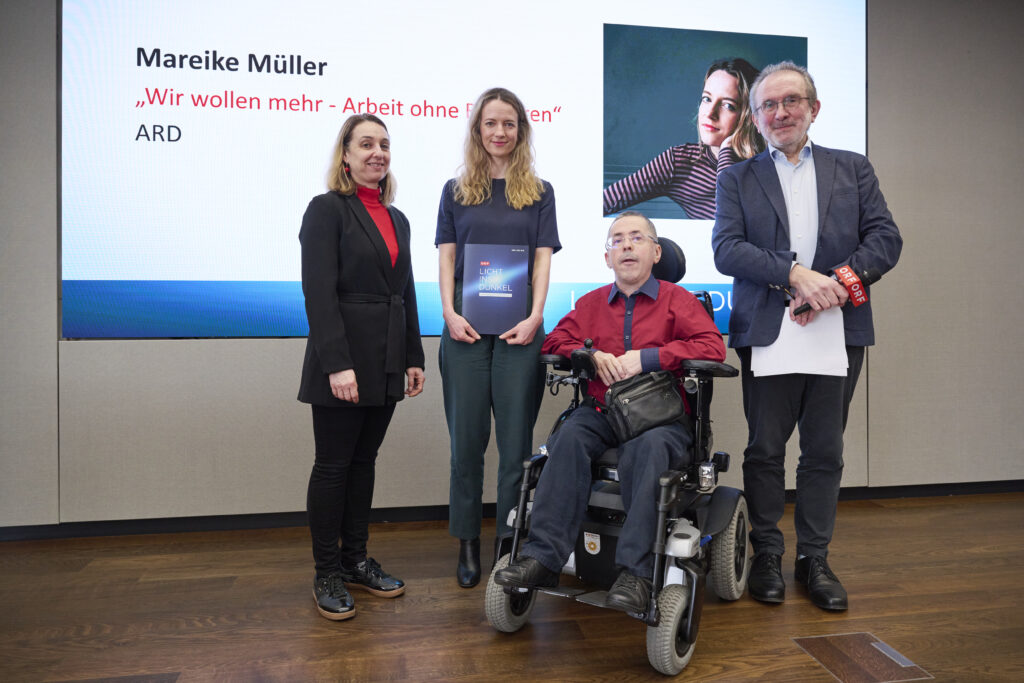 Mareike Müller erhält den Herbert-Pichler-Inklusions-Medienpreis 2026 in der Kategorie Fernsehen. Sie steht gemeinsam mit Martin Ladstätter, Fritz Hausjell und Ines Stilling auf einer Bühne vor einer Präsentationsfolie mit Titel und Porträtbild ihres Beitrags.