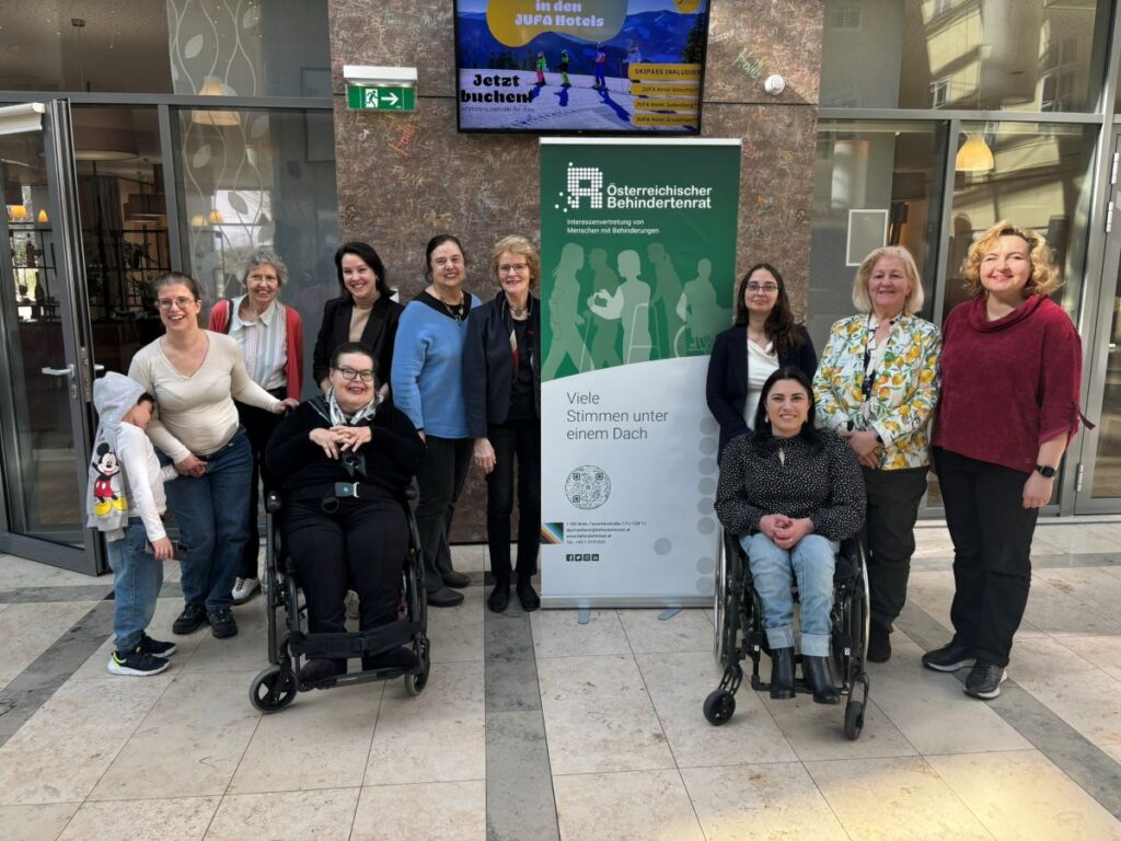 Gruppenbild von etwa 10 Frauen, einem Kind und einem Hund vor dem Rollup des Österreichischen Behindertenrats
