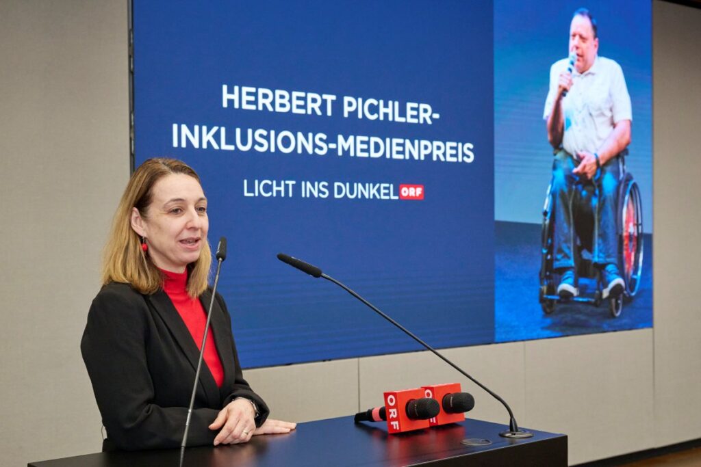 Frau mit brünettem Haar, roten Oberteil und schwarzem Blazer 