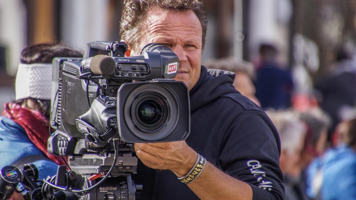 Ein Kameramann filmt mit einer professionellen Fernsehkamera mit ORF-Logo bei einer Veranstaltung im Freien. Im Hintergrund sind Menschen unscharf zu sehen. Foto: Pixabay/rottonara