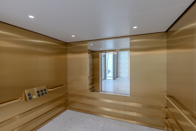 Innenraum des neuen Besucherlifts im Naturhistorischen Museum Wien mit goldfarbenen Wänden, Handläufen und Bedienfeld sowie ausreichend Platz für Rollstühle.