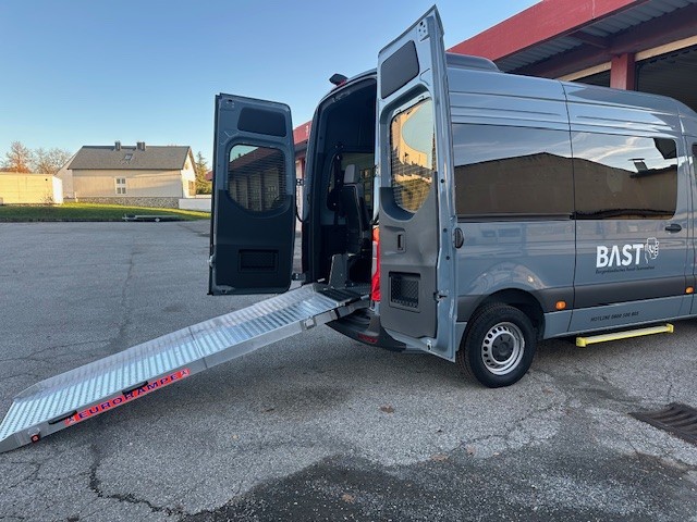 Rollstuhlgerechter Kleinbus mit geöffneter Heckklappe und ausgeklappter Rampe zum Ein- und Ausstieg auf einem Parkplatz.