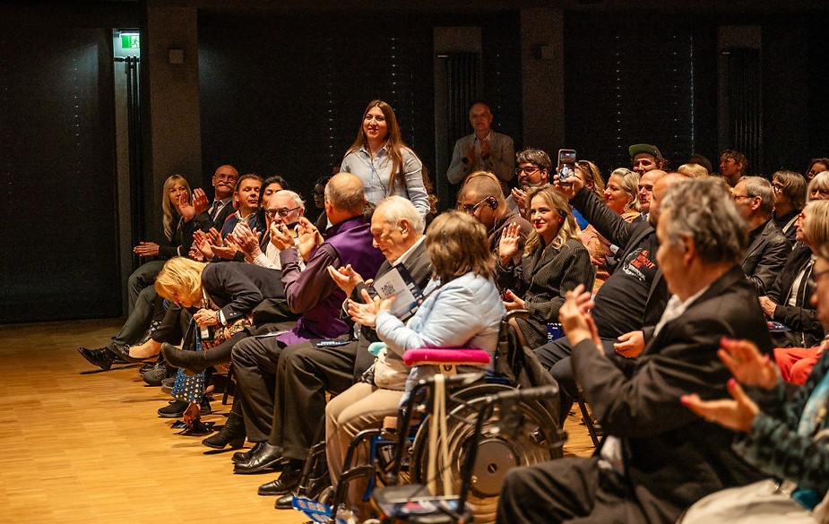 Publikum im Veranstaltungssaal des Filmfestivals ART WITHOUT LIMIT. Zahlreiche Besucher*innen sitzen auf Stühlen, einige Personen nutzen Rollstühle oder Rollatoren. Die Menschen applaudieren aufmerksam in einem modern beleuchteten Saal mit Balkon und Holzfußboden.