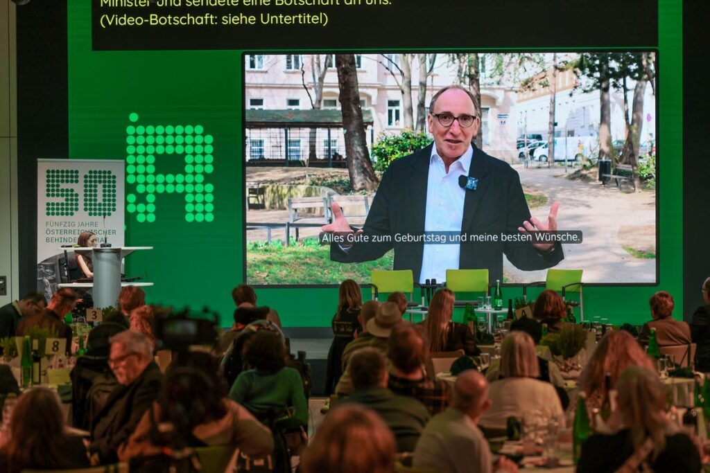 Publikum bei der Jubiläumsfeier „50 Jahre Österreichischer Behindertenrat“ während einer Videobotschaft von Bundesminister a. D. Johannes Rauch.