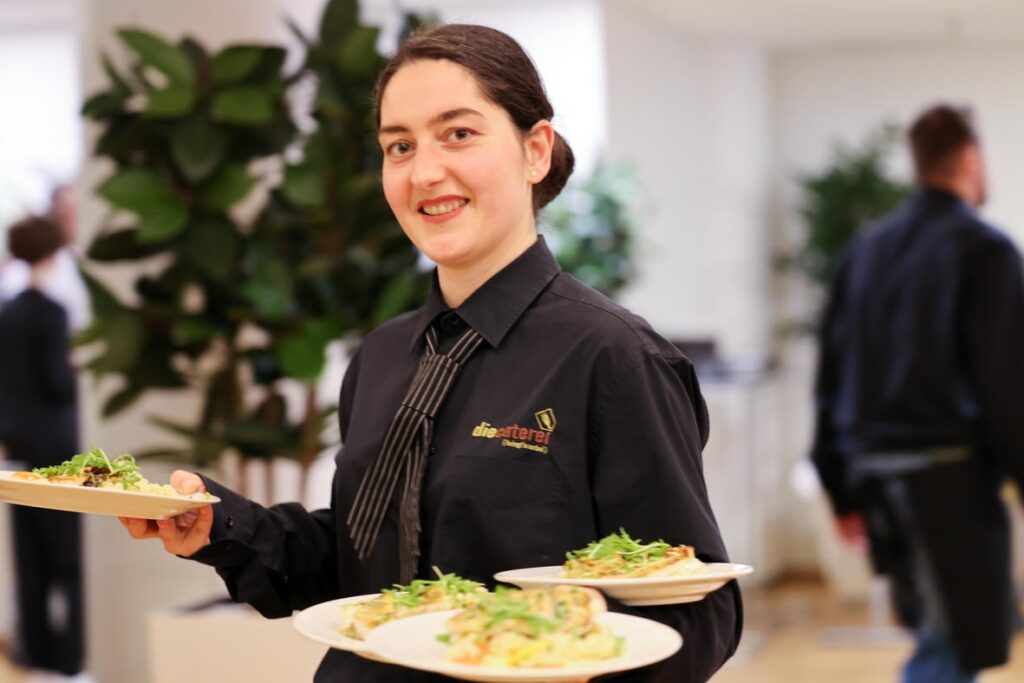 Servicekraft mit mehreren Tellern beim Catering der Jubiläumsfeier des Österreichischen Behindertenrats.