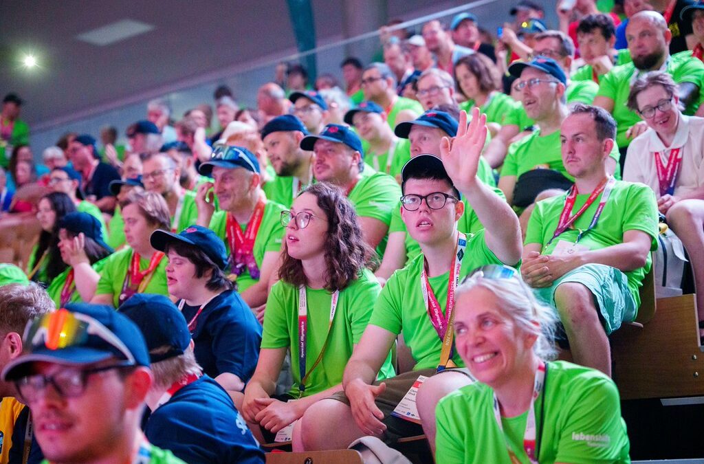Teilnehmer:innen und Betreuer:innen verfolgen die Schlussfeier der Nationalen Special Olympics Sommerspiele 2026 in der Sport Arena Wien. Ein Teilnehmer hebt die Hand, viele blicken aufmerksam zur Bühne.