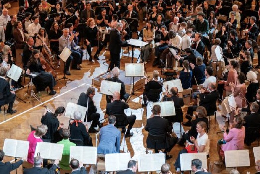 Musiker:innen eines Orchesters sitzen gemeinsam mit dem Publikum im Konzertsaal. In der Mitte dirigiert eine Person das Ensemble. Die enge Anordnung ermöglicht ein unmittelbares Konzerterlebnis für Menschen mit und ohne Behinderungen. Foto: Wiener Symphoniker/Wiener Konzerthaus.