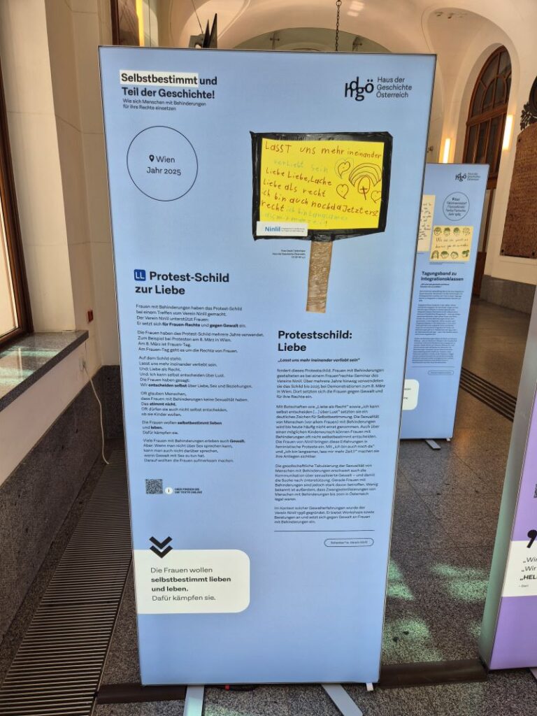 Hellblaue Ausstellungstafel mit gelbem Protestschild von Ninlil sowie Informationen zu Selbstbestimmung, Sexualität und Gewaltschutz für Frauen mit Behinderungen.
