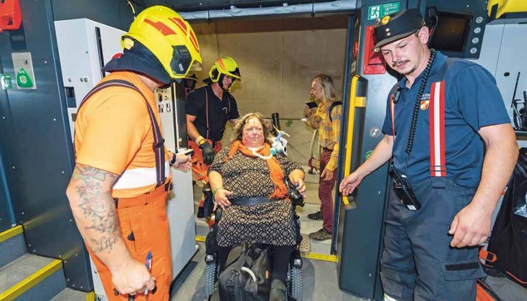 Bernadette Feuerstein verlässt mit ihrem Elektrorollstuhl einen Zug im Koralmtunnel. Einsatzkräfte der Feuerwehr und ein Mitarbeiter der ÖBB begleiten die Evakuung im Rahmen einer Notfallübung.