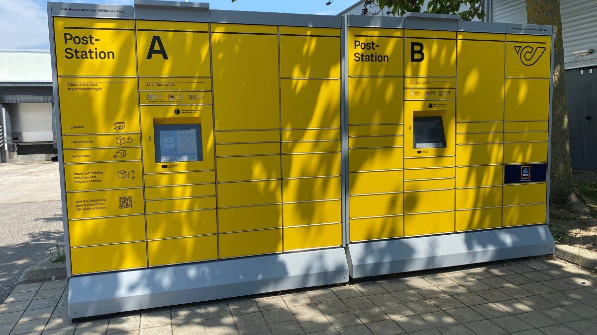 Gelbe Post-Abholstation mit mehreren Paketfächern unterschiedlicher Größe und Höhe sowie einem Bedienfeld in der Mitte.