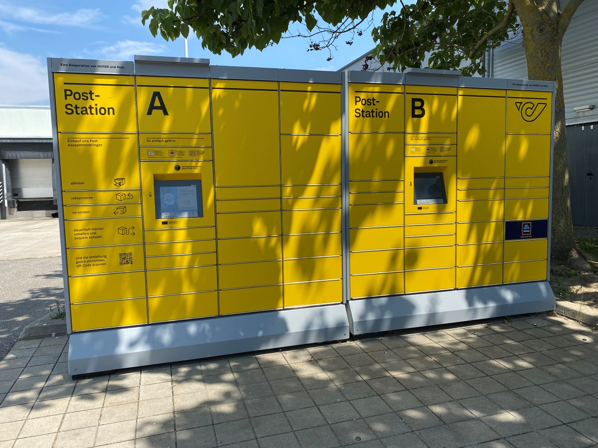 Gelbe Post-Abholstation mit mehreren Paketfächern unterschiedlicher Größe und Höhe sowie einem Bedienfeld in der Mitte.