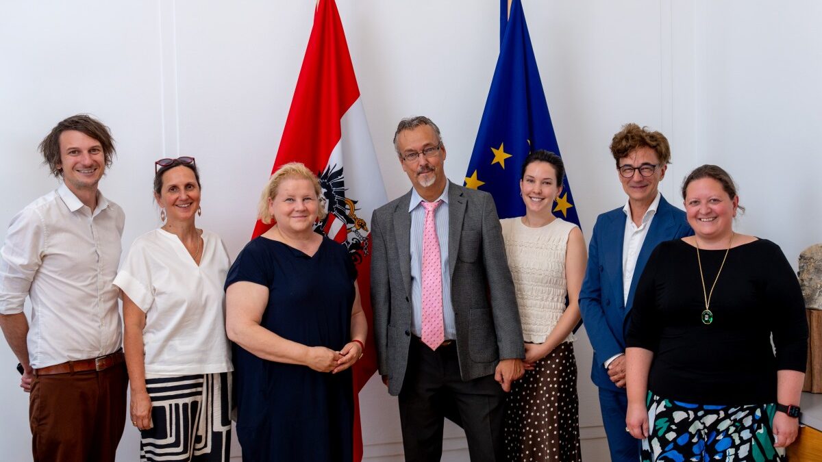 Gruppenfoto eines Treffens zwischen Vertreterinnen des Sozialministeriums und des Österreichischen Behindertenrats. Sieben Personen stehen nebeneinander vor einer weißen Wand, zwischen einer österreichischen Staatsflagge und einer EU-Flagge. In der Mitte stehen Sozialministerin Korinna Schumann und Behindertenrats-Präsident Klaus Widl. Die übrigen Teilnehmerinnen sind links und rechts davon angeordnet. Alle sind in Business- bzw. Business-Casual-Kleidung gekleidet und lächeln in die Kamera.