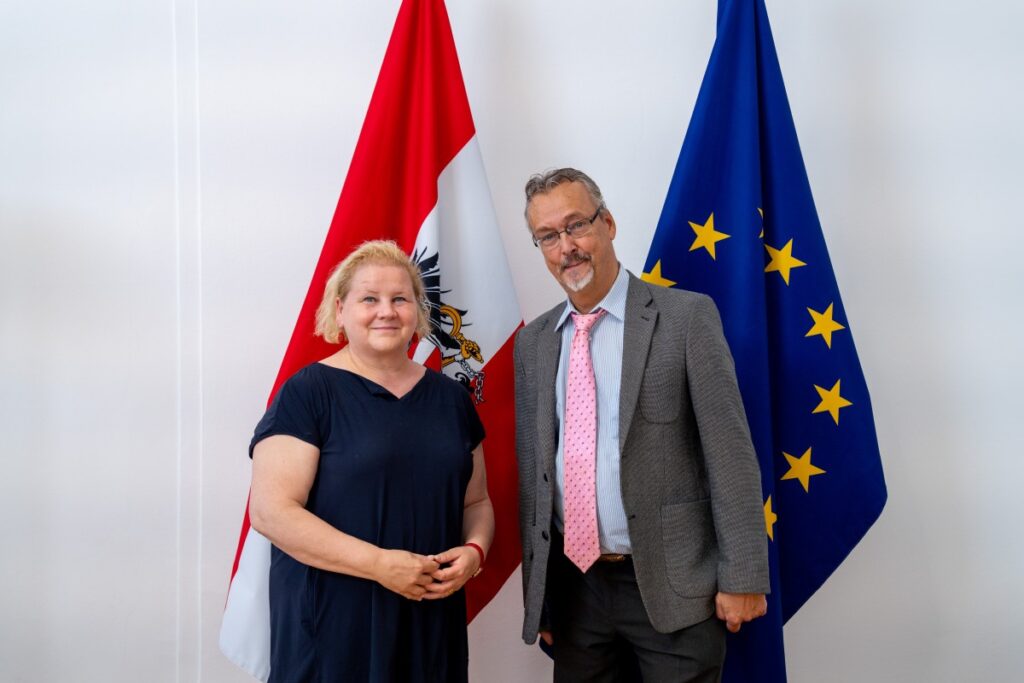Sozialministerin Korinna Schumann und Behindertenrats-Präsident Klaus Widl vor österreichischer und europäischer Flagge.