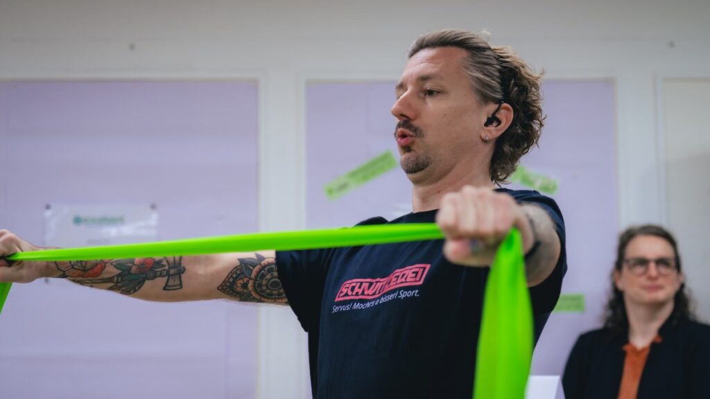 Fitnesstrainer Manfred Schütz zieht ein grünes Theraband auseinander