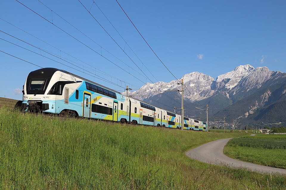 Westbahn-Zug auf einer Bahnstrecke bei Flaurling in Tirol, im Hintergrund die Tiroler Berglandschaft.