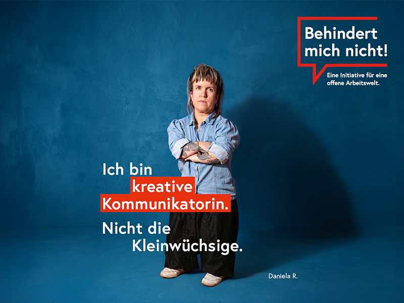 Daniela R. steht mit verschränkten Armen vor blauem Hintergrund. Daneben steht: „Ich bin kreative Kommunikatorin. Nicht die Kleinwüchsige.“