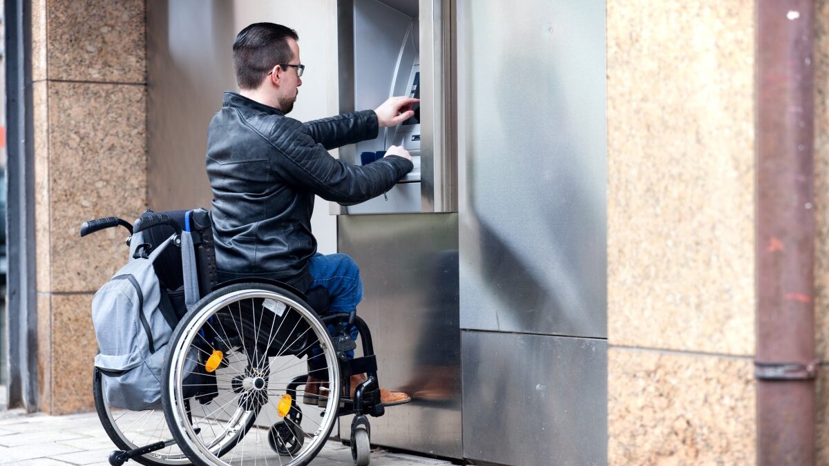 Rollstuhlnutzer hebt Geld beim Bankomat-Gerät ab.