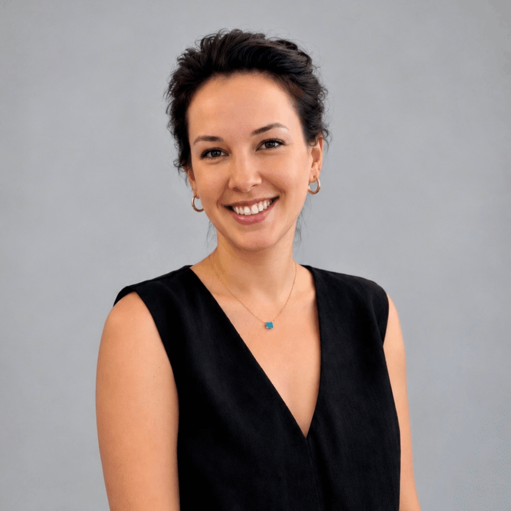 Portraitfoto von Victoria Biber. Sie hat dunkelbraune Haare, trägt eine schwarze Bluse und lächelt in die Kamera.