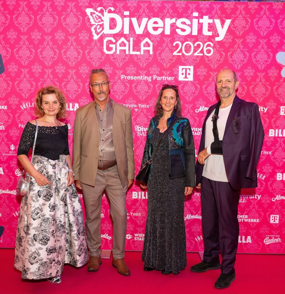 4 vor einer pinken Leinwand stehende Personen in festlicher Kleidung