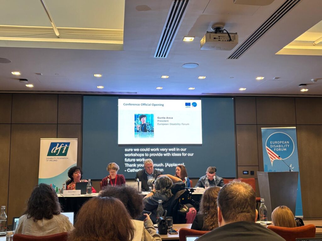 5 Personen sitzen an einem Podium und sprechen vor einem Publikum.