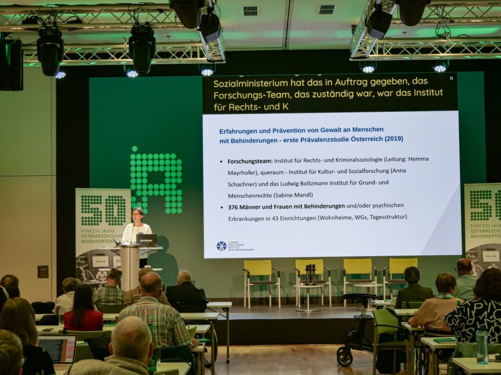 Sabine Mandl hält bei der Fachkonferenz des Österreichischen Behindertenrats 2026 einen Vortrag zum Thema „Gewaltfrei leben – ein Menschenrecht“. Sie steht am Rednerpult, hinter ihr ist die Präsentationsfolie zu sehen.