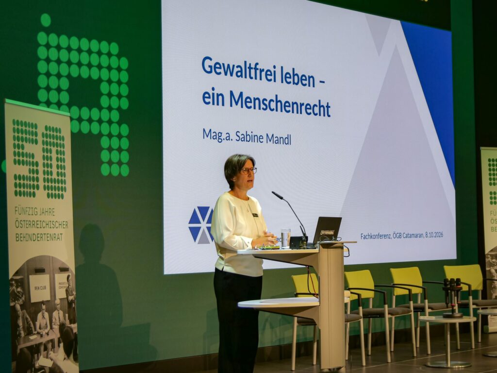Sabine Mandl hält bei der Fachkonferenz des Österreichischen Behindertenrats 2026 einen Vortrag zum Thema „Gewaltfrei leben – ein Menschenrecht“. Sie steht am Rednerpult, hinter ihr ist die Präsentationsfolie zu sehen.