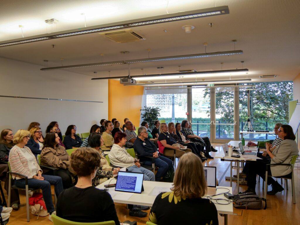 Teilnehmende der Fachkonferenz des Österreichischen Behindertenrats 2026 verfolgen die Session „Zugang zum Gewaltschutz für Frauen* mit Behinderungen“ von Heidi Egger und Lisa Udl. Die beiden Referentinnen sitzen vor der Gruppe und sprechen zu den Anwesenden.