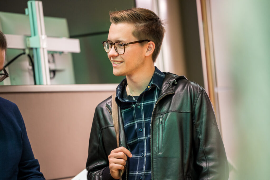 Ein lächelnder Teilnehmer der Fachkonferenz des Österreichischen Behindertenrats 2026 trägt eine Brille, eine schwarze Lederjacke und ein blau kariertes Hemd.