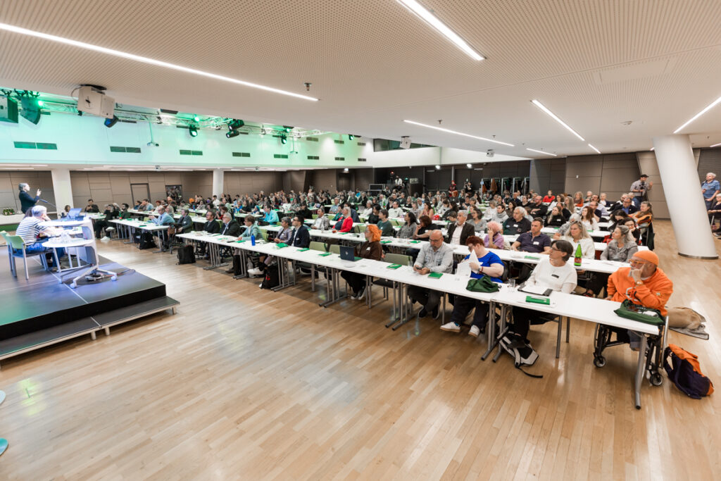 Blick auf den voll besetzten Konferenzsaal bei der Fachkonferenz des Österreichischen Behindertenrats 2026. Die Teilnehmenden verfolgen die Keynote von Ninlil, die auf der Bühne präsentiert wird.