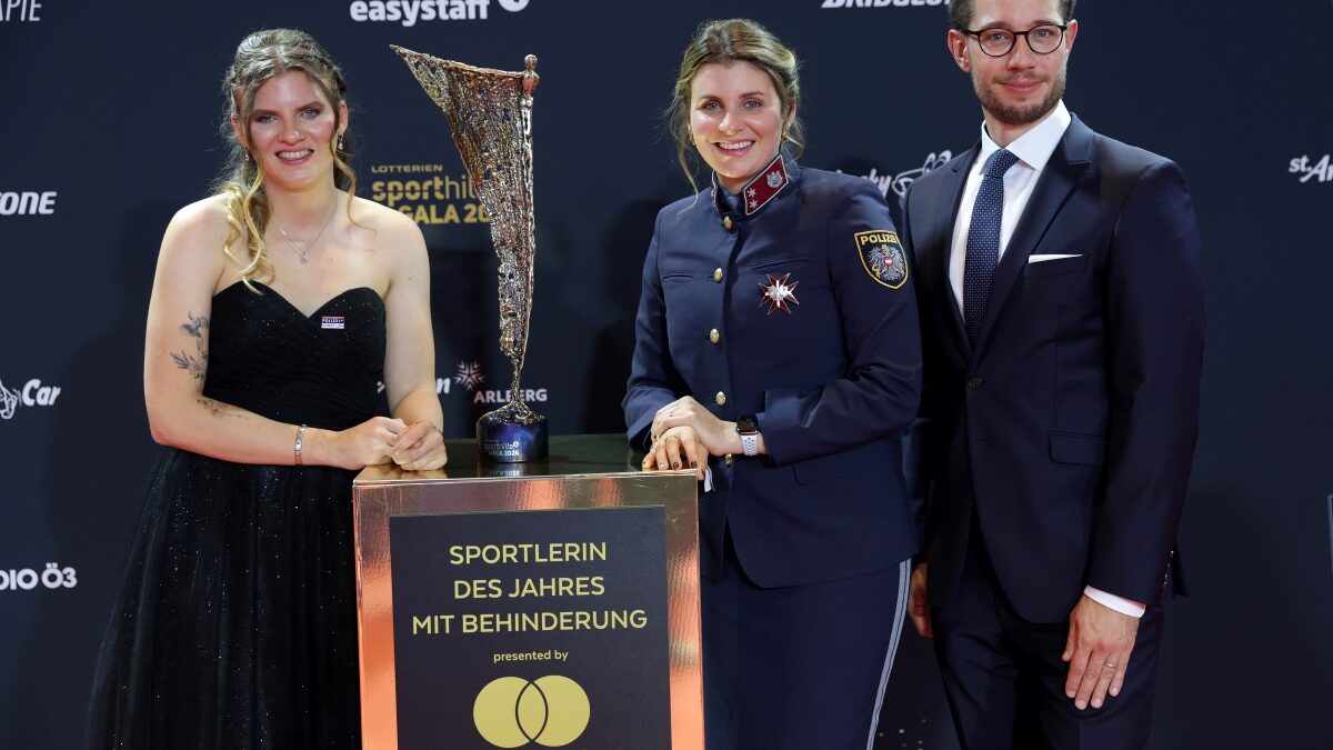 Veronika Aigner im schwarzen Abendkleid, Elisabeth Aigner in Polizeiuniform und Michael Brönner im dunklen Anzug stehen bei der Sporthilfe-Gala hinter der Auszeichnung „Sportlerin des Jahres mit Behinderung“. Zwischen ihnen steht die NIKI-Trophäe.