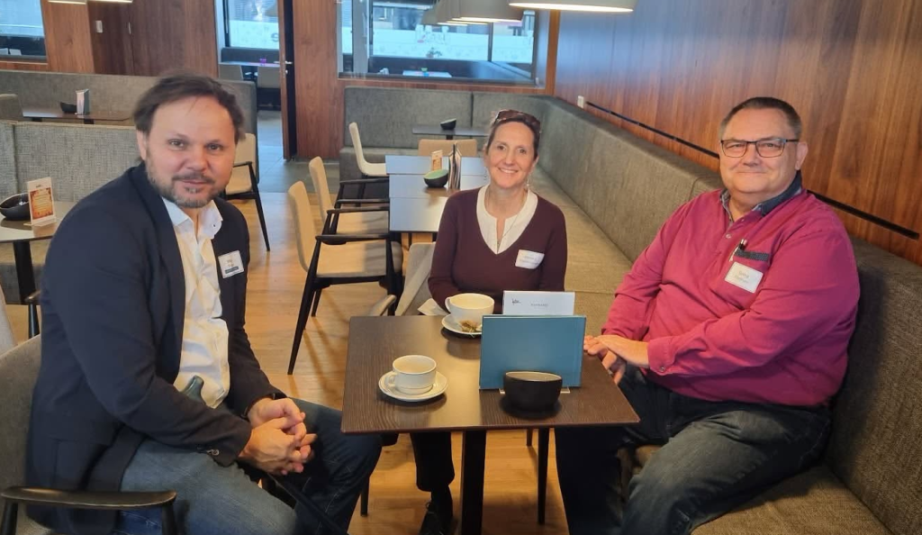 3 Personen sitzen rund um einen Tisch